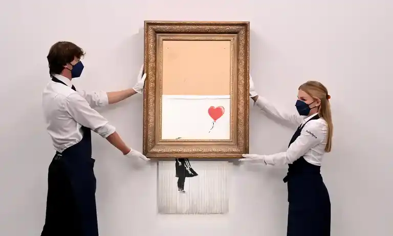 Gallery employees pose with Love is in the Bin by Banksy